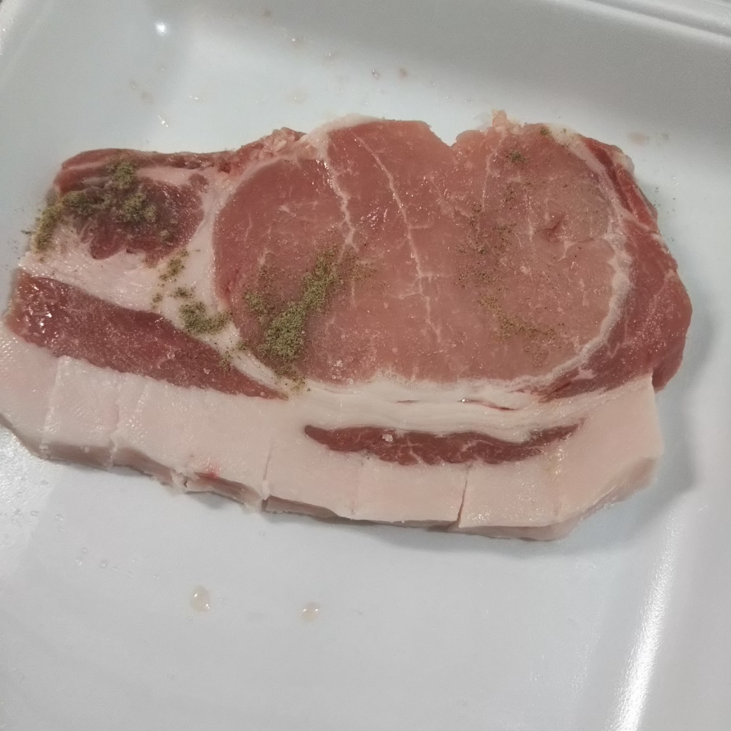豚肉のスジと脂身に包丁で切り込みを入れる。両面塩コショウをする。
