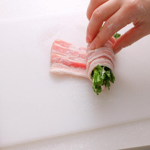 バットに薄切り豚バラ肉5枚を1/3ほど重ねながら並べていき、塩と小麦粉を全体に振りかける。手前に春菊を乗せてきっちり巻いていく。残りも同様にする。