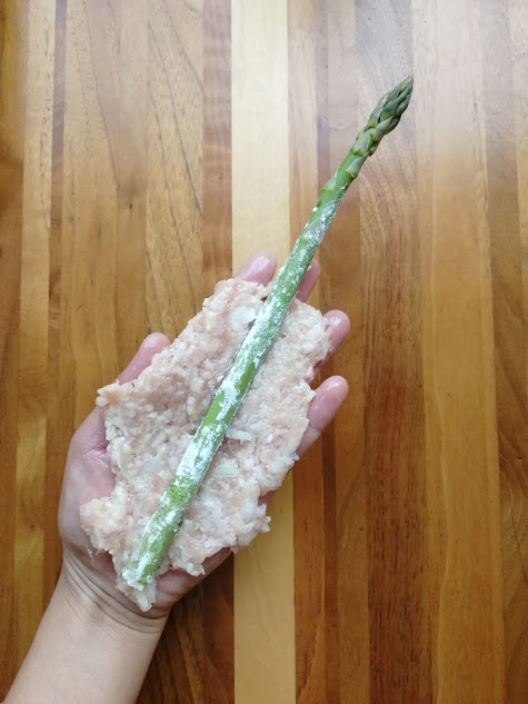 ①のつくねだねを手に広げ、包み込むようにアスパラにつける。手に油を塗ると作業がしやすい。（アスパラに油がつくとつくねだねがくっつかないので注意）