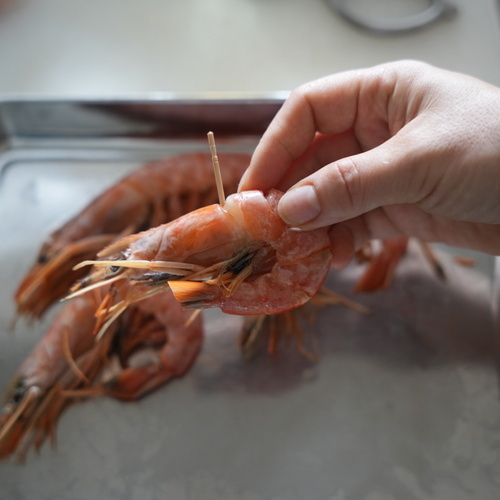 有頭えびはひげや足、尾のとがった部分をキッチンバサミで切り、背ワタを取り除いたらえびが「つ」の形になるように曲げて爪楊枝で止める。