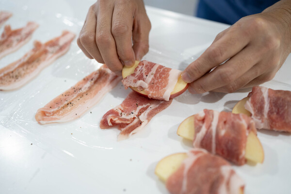 ラップの上に豚肉を並べ、片面に塩、黒こしょう少々をふる。りんごをしっかりと巻き、片栗粉を薄くまぶす。