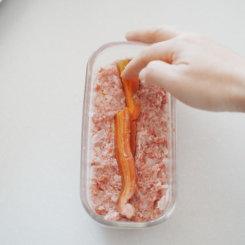 容器にオーブンシートを敷き、肉だねを1㎝の高さになるまで広げ入れる。
ベビーコーン、にんじん、アスパラガスをバランスよく並べ、都度肉だねを詰める。