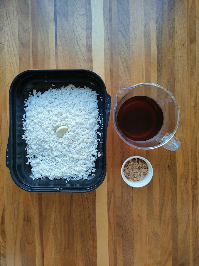 マルチグリルキャセロールに水けをきった米とにんにくを入れる。しょうゆ・白だし・みりんを計量カップに入れる。