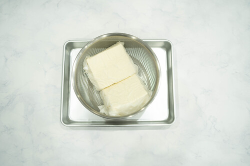 豆腐を２ｃｍの厚さに切り、フライパンや鍋にいれ、水をかぶるくらい注いだら、中火にかけ沸騰したら、ザルに取り出し水気をきる。