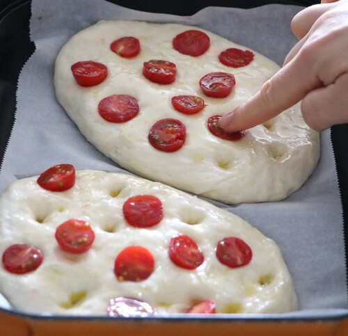 フォカッチャの生地に指でくぼみを作り、1枚につきオリーブオイル小さじ1ずつと塩をかける。ミニトマトは半分に切り、くぼみに埋めこむ。ピザ用チーズをかける。