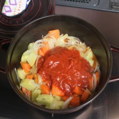 トマト缶を細かくカットして加え、②の肉も戻し入れ蓋をして弱火でさらに20分加熱する。