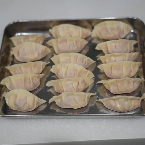 餃子の皮にタネをのせてヒダをつけて包む。