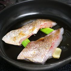 フライパンにねぎの青い部分、薄切りにしたしょうがを置き、その上に白身魚を並べる。