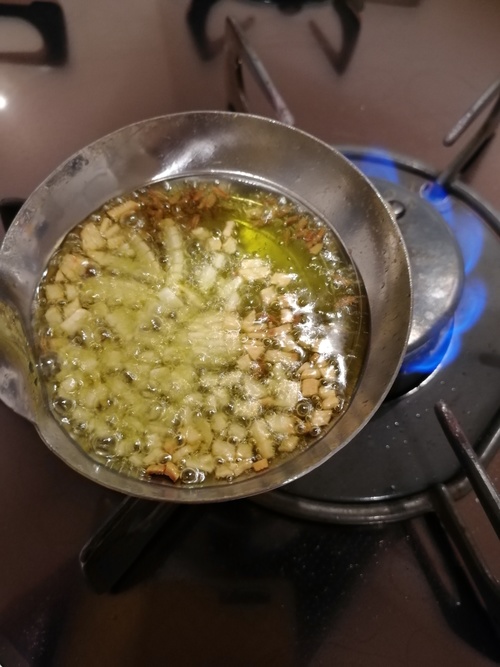 お玉にオリーブオイル、みじん切りにしたにんにく・クミンシードを入れて、直火にかけ、にんにくがキツネ色になるまで加熱する。