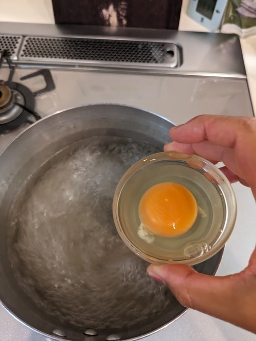 小鍋に湯を沸かし（約500ml）、酢大さじ2と塩小さじ1を入れ、グルグル回して水流で渦を作る。卵はカップに割り入れておく。
