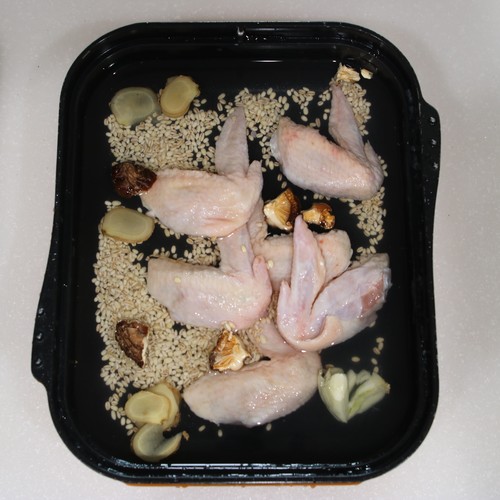 マルチグリルのキャセロールに鶏手羽先、にんにく、しょうが、もち麦を入れ、干ししいたけを手で割り入れる。