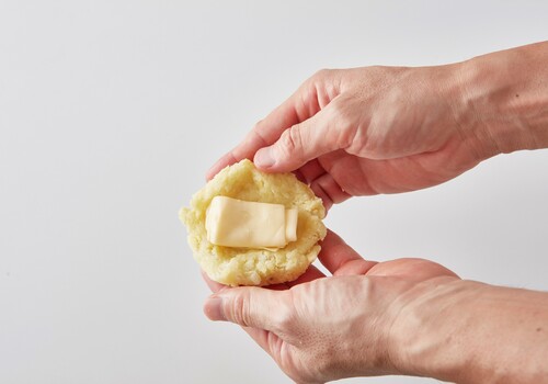 ４等分にして、丸めたら、折りたたんだスライスチーズを包み、少しつぶしたら、表面にベーコンを張り付ける。